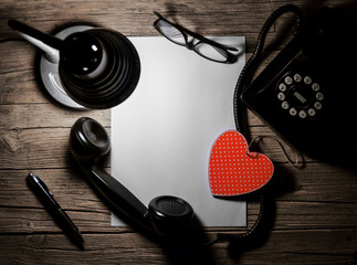 Retro telephone, red wooden heart and a blank sheet of paper.