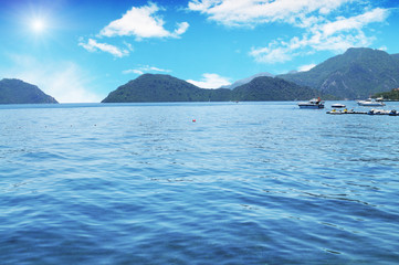 Boats, yachts and jet ski in the sea with mountains and sky with sun