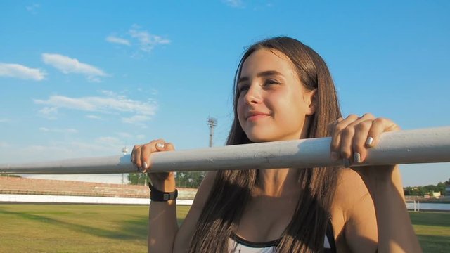 Beautiful girl engaged in fitness at the stadium. The girl pulls up on the bar.