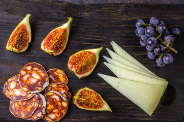 Cheese figs, grapes, chorizo over black grunge background