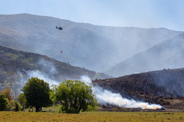 A helicopter dampens down hot spots during a controlled scrub fire to clear farmland of gorse and...