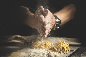 chef men hands with flour splash over the table. preparation of fresh homemade pasta on a black...