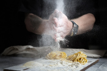 chef men hands with flour splash over the table. preparation of fresh homemade pasta on a black...