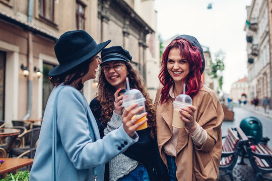 Three female friends having drinks outdoors. Women clinking coffee, orange juice and tea cups