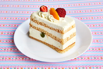 Piece of fruit yogurt cake with fresh strawberry, raspberry, peach, grapes and almonds on a white plate and pattern background. Close up.