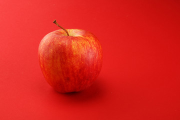 Ripe red apple with leaves on red background.