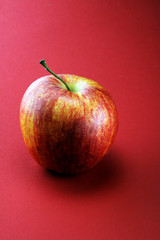 Ripe red apple with leaves on red background.