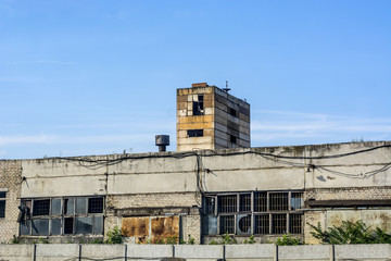 An old building of blocks and white brick with broken windows, abandoned production against a blue sky