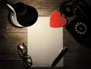 Retro telephone, red wooden heart and a blank sheet of paper.