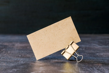 Business card from craft recycled paper with metal binder clip on table. Cardboard business card on dark background.