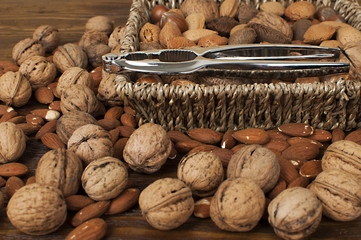 different kind of nuts in straw basket on wooden table with nutcracker