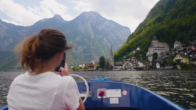 young woman riding boat taking pictures of famous village Hallstatt mountain lake