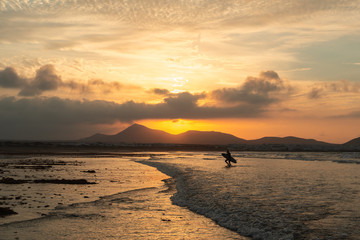 silhouette of a surfer coming out of the ocean on a background of sunset and mountains