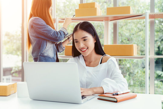 Business owner concept. Young two asian woman smiling happy using laptop working and checking customers online order products packaging in modern home office