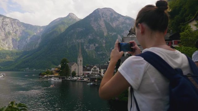 back view from young woman taking pictures at famous Hallstatt mountain lake