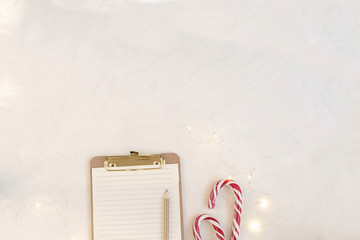 Christmas planning concept - workspace mockup, clipboard with blank paper, candy canes, garland lights