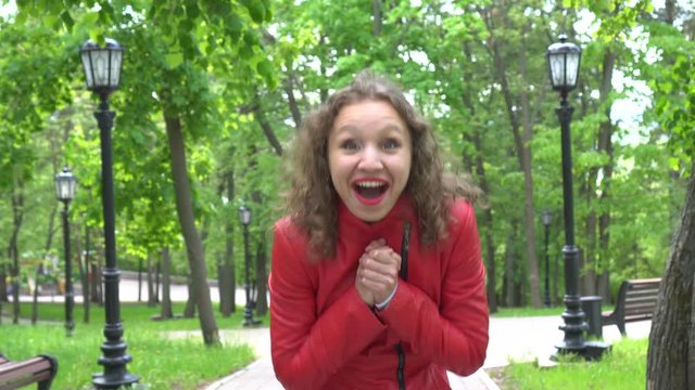 Surprised woman in red leather jacket looking at camera and surprising, outdoors over summer park