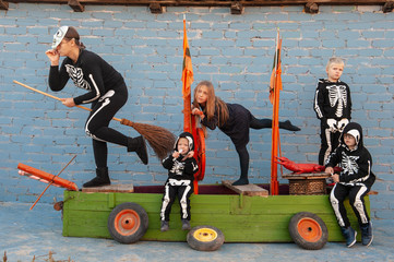 cute family in skeleton costumes for Halloween celebrations are playing pirates on wooden sailing ship. Boys, girl and mother are happy together. Masks pumpkin and dead man.