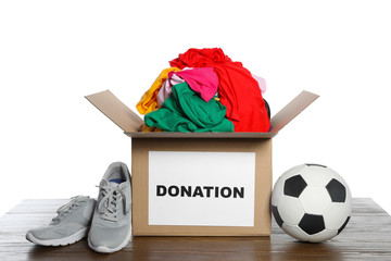 Donation box with clothes, shoes and soccer ball on table against white background