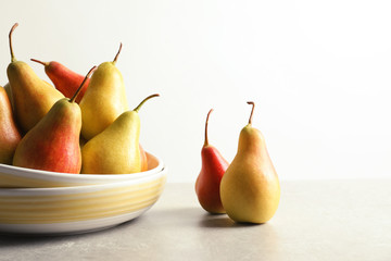 Plate with ripe pears on table against light background. Space for text
