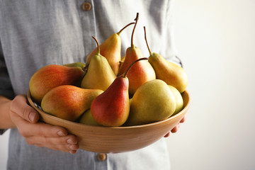 Woman holding bowl with ripe pears on light background, closeup