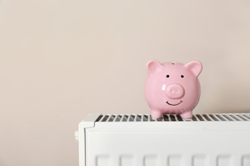 Piggy bank on heating radiator against light background. Space for text