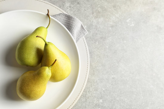 Plate with ripe pears on light background, top view. Space for text