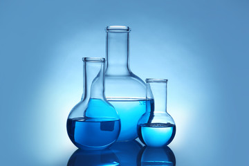 Flasks with liquid on table against color background. Laboratory analysis