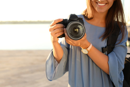 Young female photographer holding professional camera at pier, closeup. Space for text