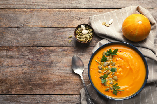 Flat lay composition with pumpkin cream soup in bowl on wooden background. Space for text