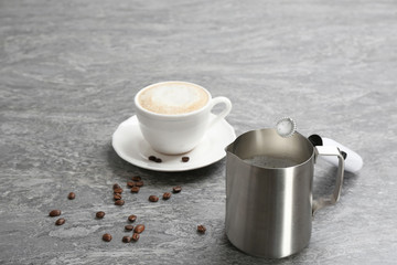 Milk frother, pitcher and cup of coffee on table