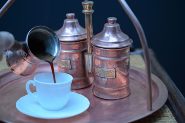 pouring coffee from a pots into a white Cup next to the copper coffee making facilities