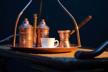 a Cup of coffee near the sugar bowl and a container with coffee on a copper tray and a rattan table