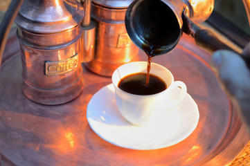 pouring coffee from a pots into a white Cup next to the copper coffee making facilities