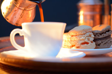 pouring coffee from a pots into a white Cup next to the copper coffee making facilities and macaroons