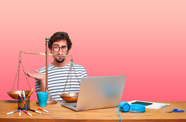 young crazy graphic designer on a desk with a laptop and with a justice balance or scale