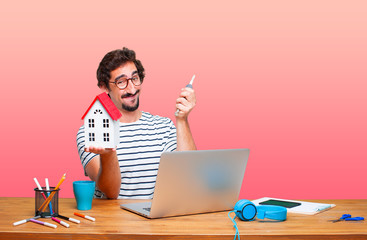 young crazy graphic designer on a desk with a laptop and with a house model