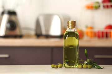 Bottle of olive oil on table against blurred background. Space for text