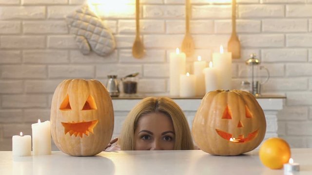 Funny mom hiding under table with carved pumpkins, scaring her family, pranks