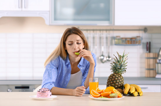 Woman choosing between dessert and fruits at table in kitchen. Healthy diet