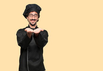 young crazy man as a chef smiling with a satisfied expression showing an object or concept with...