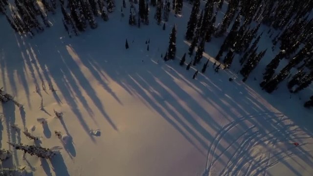 Tilt down aerial, skiers descend down slope at sunset
