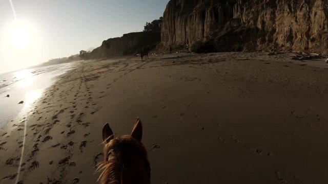Slow motion POV, riding horseback on beach at sunset