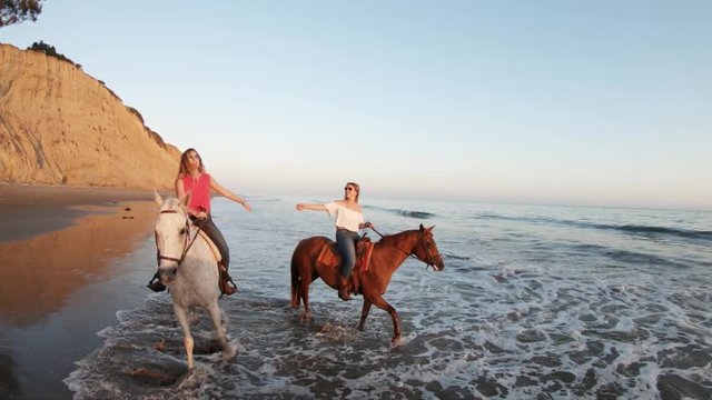 Female horseback riders on beach at sunset, slow motion