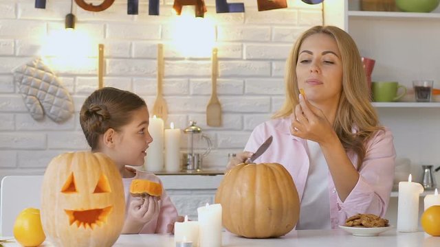 Little daughter excitedly watching her mother tasting pumpkin during carving