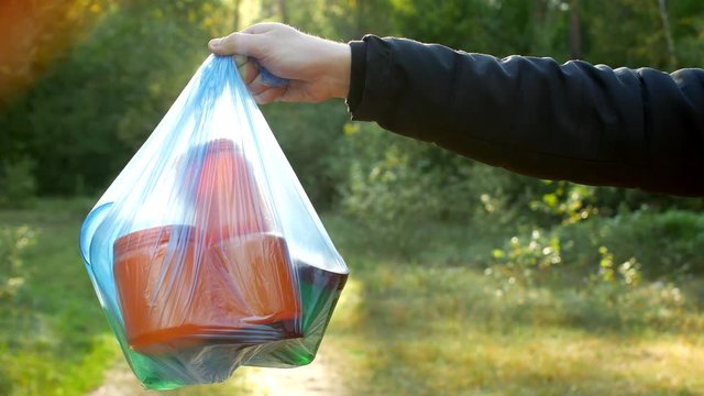 A man holds a package with garbage in his hand against the background of the forest and nature, garbage and nature, pollution of nature, close-up