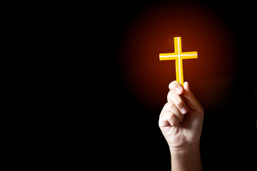 Human hand holding and lift of christian cross with light black background