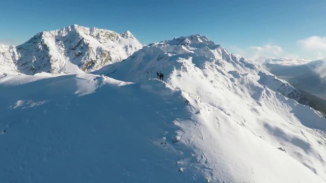 People hike on snowy mountain ridge, wide aerial