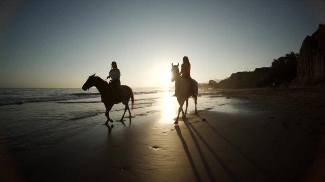Sunset over horseback riders on beach, slow motion