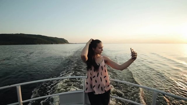 A beautiful girl makes selfie while standing on a ships bow in front of the scenic view